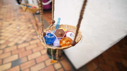 Pequeña cesta colgante elaborada en fibras naturales que contiene diversos objetos coloridos.