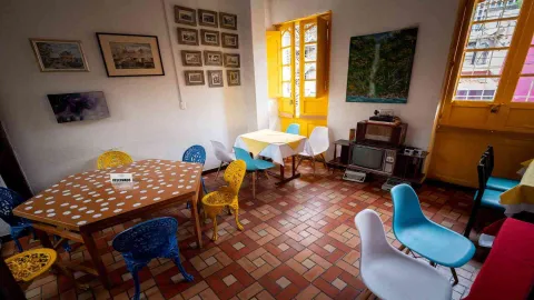 Área con una mesa de lunares y otra con mantel amarillo. Incluye un televisor antiguo sobre un mueble y sillas de colores.