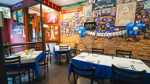 Vista en ángulo de mesas de madera vestidas de blanco y azul dispuestas junto a la pared decorada con fotografías.