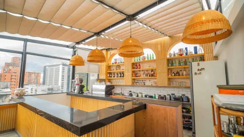 Barra de bar en la terraza superior con acabado acanalado de madera, techo retráctil y estantes iluminados con botellas.