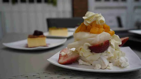 Postre de merengón con crema batida, fresas frescas y trozos de mango servido en plato blanco sobre una mesa. 