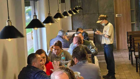 Mesero tomando un pedido a clientes sentados en el comedor iluminado por lámparas colgantes en Kuty. 