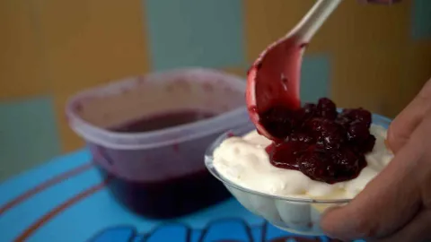 Mano sirviendo mermelada artesanal de mora sobre copa con crema de postre. 