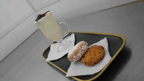Bandeja negra con una copa de postre, un alfajor con coco y una galleta horneada sobre servilletas. 