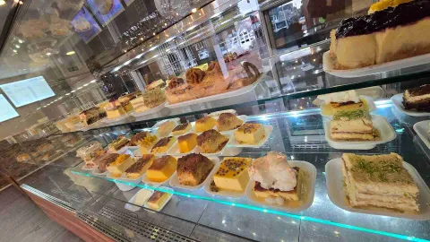 Vista panorámica de mostrador refrigerado con repisas llenas de tortas, flanes y postres individuales. 