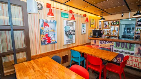 Mesas de madera con sillas de colores, lámparas rojas y pósteres musicales retro en pared decorada del interior.