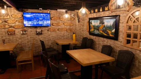 Comedor con mesas de madera, paredes tipo piedra, réplicas de fachadas y un cuadro de paisaje rural. 