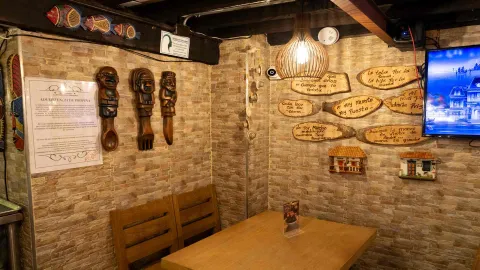 Rincón del restaurante con mesa de madera, lámpara de mimbre, maderas con refranes y esculturas étnicas. 