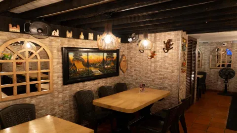 Salón con mesas, lámparas colgantes de madera, espejo con marco de ventana y pintura de un atardecer rural. 