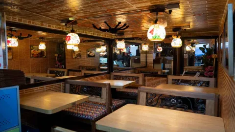 Comedor con mesas de madera, sillas labradas, lámparas de cristal decoradas y espejos que reflejan el salón. 