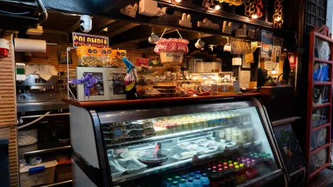 Mostrador con vitrina iluminada de postres, bebidas, letreros de Colombia y paquete de dulces típicos.