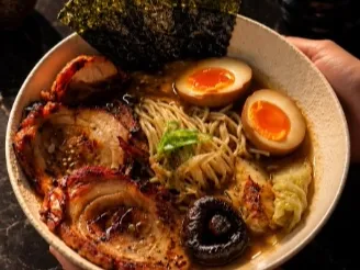 Ramen servido en un tazón, con fideos, cerdo, huevo, hongos y alga nori.