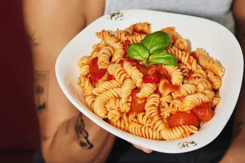  Pasta fusilli con salsa de tomate, tomates cherry y hojas frescas de albahaca, servida en un plato blanco.