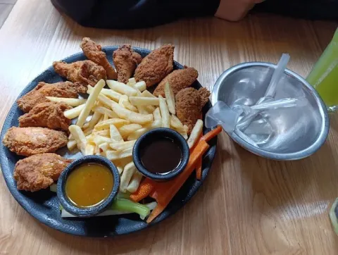 Selección de pollo apanado y papas fritas, acompañada de salsas y vegetales frescos.