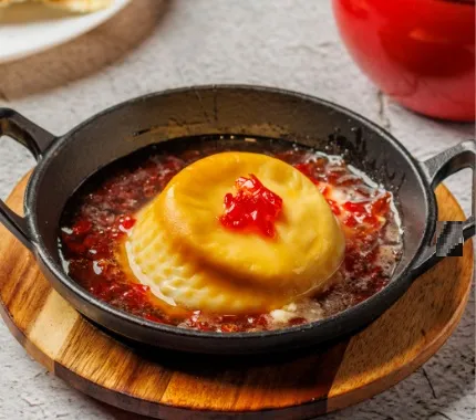 Preparación de pasta rellena servida en sartén, acompañada de salsa de tomate y queso fundido.