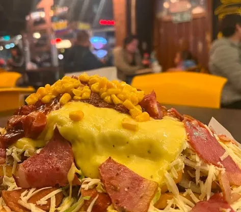 Salchipapa cubierta con salchicha, queso fundido, maíz y salsa de la casa.