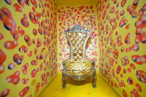 Salón amarillo del Museo de la Selfie en Bogotá, con paredes y piso decorados con numerosas formas circulares de colores. En el centro se encuentra un llamativo trono dorado con detalles ornamentales, dispuesto como escenario para fotografías.