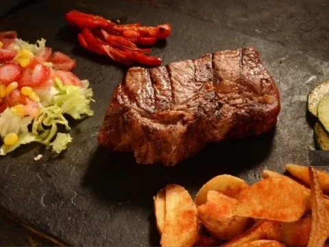 Corte de carne a la parrilla acompañado de ensalada, papas y vegetales.