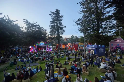 Festival gastronómico nocturno con música en vivo, restaurantes y público reunido en un parque.
