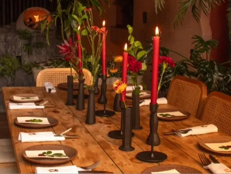 Mesa de restaurante decorada con velas, flores y vajilla, en un ambiente cálido y sofisticado.