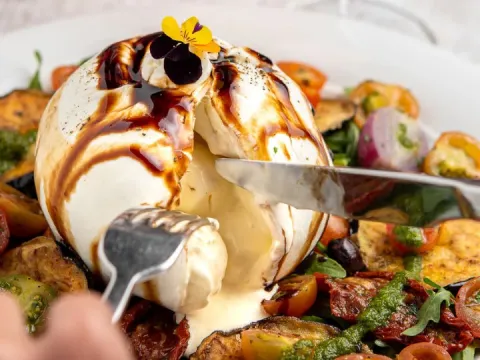Burrata cremosa bañada con reducción de balsámico, acompañada de vegetales y tomates.