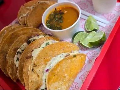 Selección de tacos de birria acompañados de consomé y limón.
