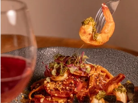 Plato de mariscos con camarones, vegetales y hierbas frescas, acompañado de una copa de vino.