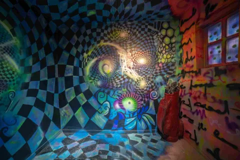 Espacio inmersivo del Museo de la Selfie en Bogotá, decorado con murales psicodélicos en tonos azules, verdes y morados. Las paredes y el piso presentan patrones geométricos que crean un efecto visual de movimiento, acompañado de elementos decorativos y luces de colores.