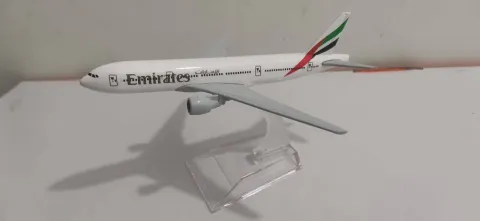 Avión comercial a escala de Emirates, con fuselaje blanco, motores bajo las alas y los característicos colores de la aerolínea en la cola. La maqueta está exhibida sobre una base transparente, ideal para los amantes de la aviación y el coleccionismo.