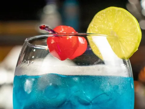 Cóctel azul servido con hielo, cereza y rodaja de limón.