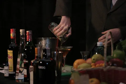  Persona preparando un cóctel con bebidas, frutas y utensilios de bar.