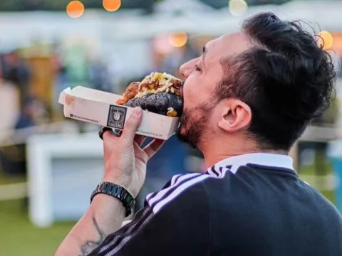  Hombre disfrutando de una hamburguesa durante un festival gastronómico al aire libre.
