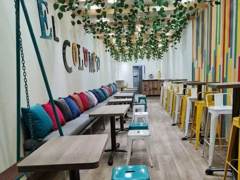 Salón de El Columpio con mesas, sillas coloridas y decoración vegetal.