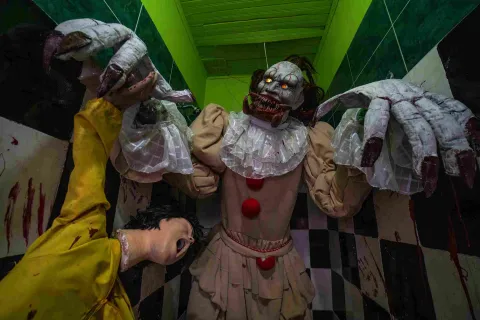 Escenario de terror del Museo de la Selfie en Bogotá, con una figura de payaso siniestro en el centro, acompañada por criaturas de aspecto monstruoso con grandes manos y rostros aterradores. El espacio está ambientado con paredes verdes, un piso de cuadros blancos y negros y elementos que recrean una escena de horror.