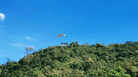 Un parapente de colores se eleva sobre una montaña cubierta de vegetación, ofreciendo una experiencia de aventura y una vista privilegiada del paisaje.