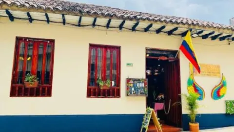  Casa de arquitectura colonial con ventanas de madera roja, tejado y bandera colombiana en la entrada principal.  