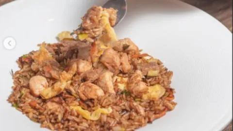 Plato hondo blanco con arroz wok salteado con trozos de pollo, carne y huevo, sostenido ligeramente por un tenedor.  