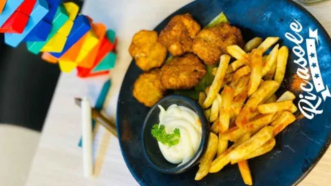 Plato servido con papas a la francesa, bocados de pollo empanizado y salsa acompañados de una torre de madera. 