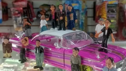 Un llamativo carro clásico de color fucsia exhibe una colección de pequeñas figuras decorativas de personajes caricaturescos, una combinación que evoca nostalgia, creatividad y pasión por los objetos coleccionables.