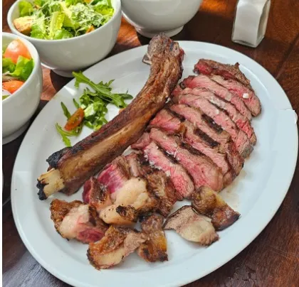 Corte de res a la parrilla en láminas, acompañado de ensalada fresca y vegetales.