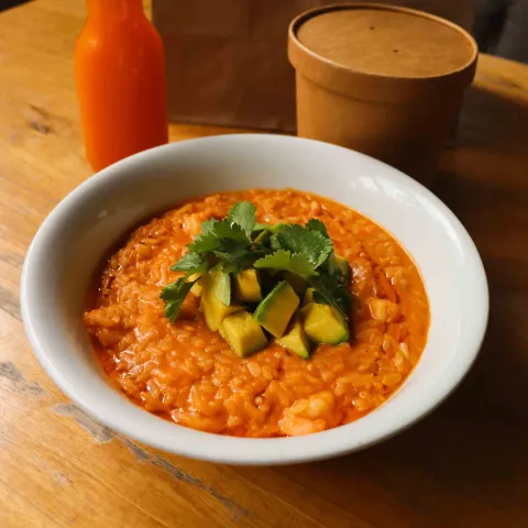 Plato de arroz cremoso con camarones, aguacate y cilantro fresco, servido en un tazón blanco sobre una mesa de madera.