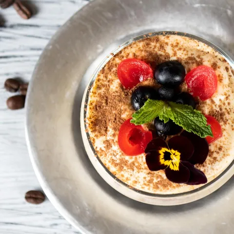 Postre cremoso tipo tiramisú, decorado con frutos rojos, arándanos y menta fresca.