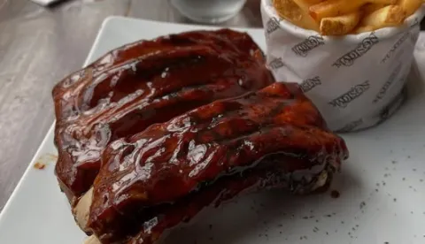 Costillas de cerdo bañadas en salsa BBQ, acompañadas de papas fritas.