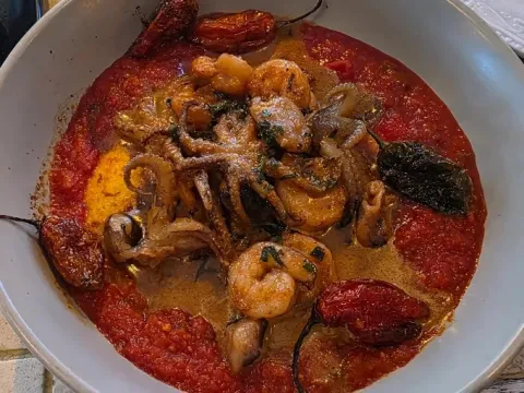 Preparación de mariscos y vegetales salteados, acompañados de tomates y una salsa de textura cremosa.