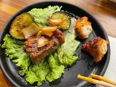 Selección de carnes a la parrilla acompañadas de lechuga y vegetales, servidas en un plato negro.