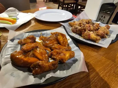 Alitas de pollo con diferentes salsas, servidas en bandejas para compartir.
