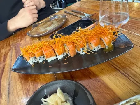 Roll de sushi con salmón, arroz y cobertura crujiente, servido en un plato negro.