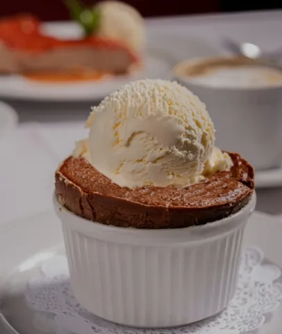 Postre de chocolate horneado, servido en un recipiente individual y acompañado de una bola de helado de vainilla.