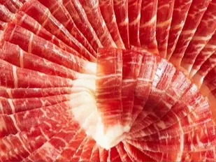 Láminas finas de jamón curado italiano dispuestas en forma circular sobre un plato.