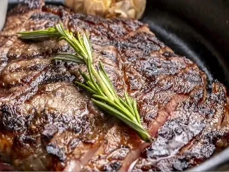 Corte de carne a la parrilla, marcado a fuego y acompañado de una rama de romero fresco.